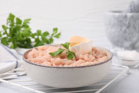 Téléchargez les photos : Viande hachée crue fraîche, persil et oeuf dans un bol sur une table gris clair, gros plan - en image libre de droit