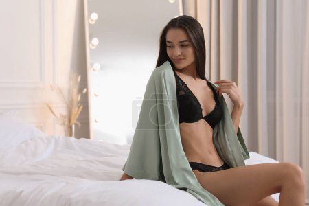 Foto de Mujer joven en ropa interior elegante negro y bata en la cama en el interior. Espacio para texto - Imagen libre de derechos