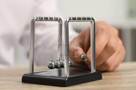 Photo for Man playing with Newton's cradle at wooden table, closeup. Physics law of energy conservation - Royalty Free Image