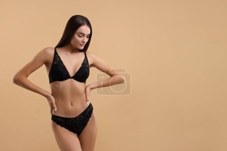 Young woman in elegant black underwear on beige background. Space for text