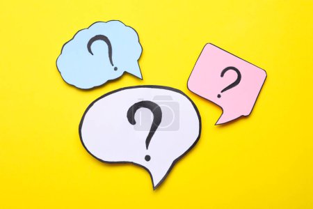 Photo for Different paper speech bubbles with question marks on yellow background, flat lay - Royalty Free Image