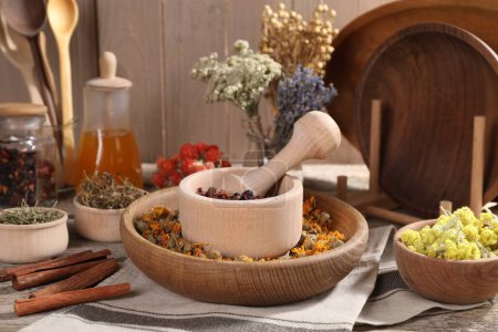 Photo for Mortar with pestle, many different dry herbs, flowers and cinnamon sticks on wooden table - Royalty Free Image