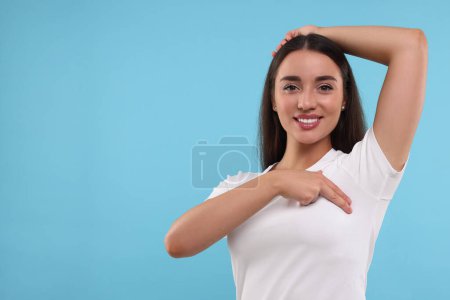 Beautiful happy woman doing breast self-examination on light blue background, space for text