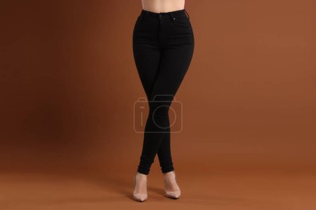 Woman wearing stylish black jeans and high heels shoes on brown background, closeup