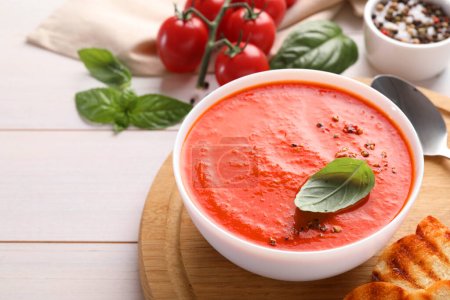 Deliciosa sopa de tomate servida sobre mesa de madera blanca, espacio para texto