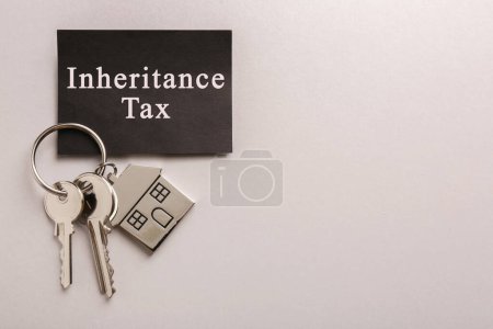Tarjeta con frase Herencia Impuesto y llaves con llavero en forma de casa sobre fondo gris, vista superior. Espacio para texto