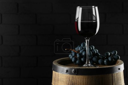 Szkło z pysznym winem i świeżymi winogronami na drewnianej beczce pod ciemną ścianą, miejsce na tekst
