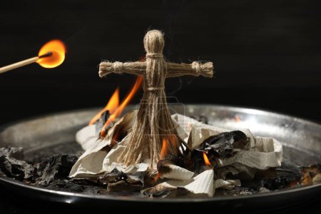 Voodoo-Puppe brennt in Metallschale auf dunklem Hintergrund. Fluch-Zeremonie