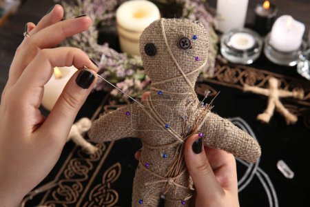 Photo for Woman stabbing voodoo doll with needle at table, closeup. Curse ceremony - Royalty Free Image