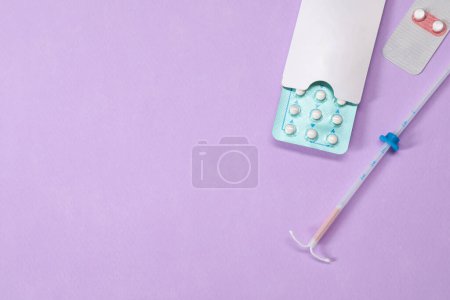 Contraception choice. Pills and intrauterine device on violet background, flat lay. Space for text