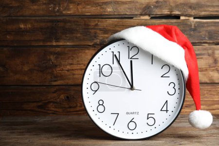Photo for Clock with Santa hat showing five minutes until midnight on wooden background, space for text. New Year countdown - Royalty Free Image