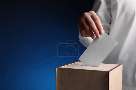 Photo for Woman putting her vote into ballot box on dark blue background, closeup. Space for text - Royalty Free Image