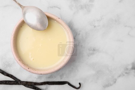 Téléchargez les photos : Bol avec lait condensé, gousses de vanille et cuillère sur table en marbre blanc, plat. Espace pour le texte - en image libre de droit