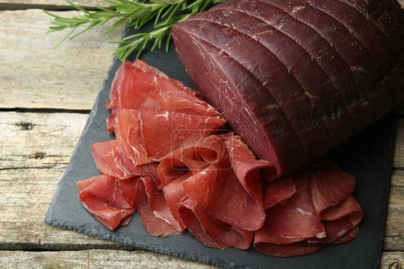 Photo for Tasty bresaola and rosemary on wooden table, closeup - Royalty Free Image