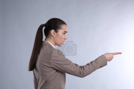 Mujer emocional en traje apuntando con el dedo índice sobre fondo gris claro