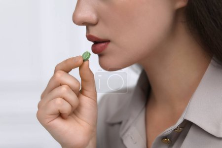 Woman taking antidepressant pill on light grey background, closeup