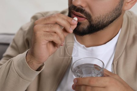 Man with glass of water taking antidepressant pill on blurred background, closeup