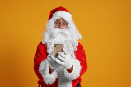 Frohe Weihnachten. Weihnachtsmann mit Smartphone auf orangefarbenem Hintergrund