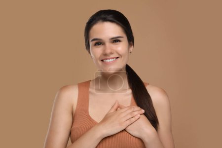 Thank you gesture. Beautiful grateful woman holding hands near heart on brown background