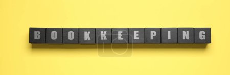 Word Bookkeeping made with black cubes on yellow background, top view