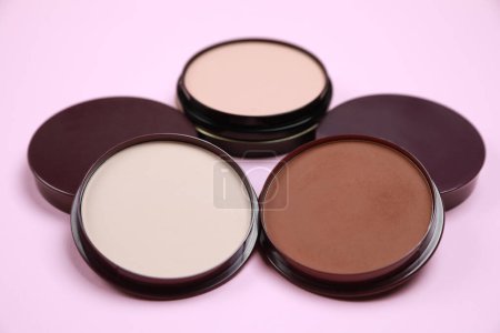 Different face powders on pink background, closeup