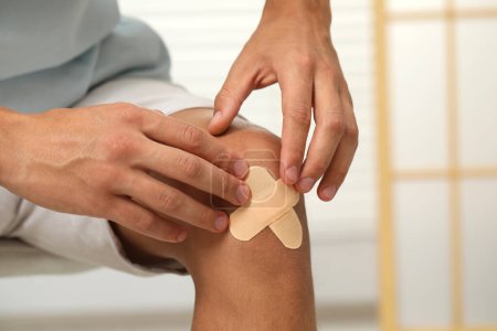 Man putting sticking plasters onto knee indoors, closeup