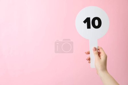 Femme tenant vente aux enchères pagaie avec le numéro 10 sur fond rose, gros plan. Espace pour le texte
