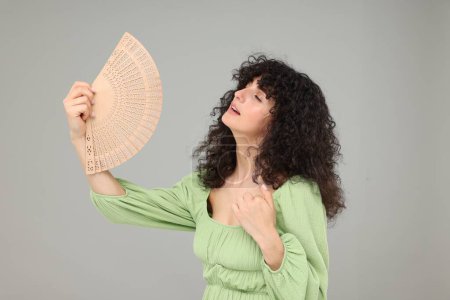 Woman with hand fan suffering from heat on light grey background