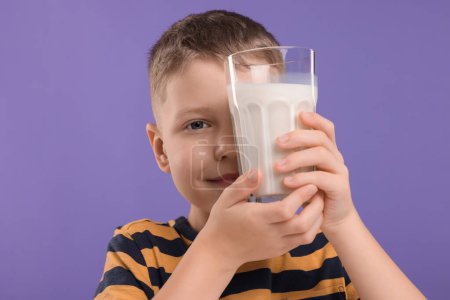 Téléchargez les photos : Mignon garçon avec un verre de lait frais sur fond violet - en image libre de droit