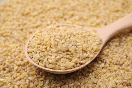 Wooden spoon and uncooked organic bulgur as background, closeup