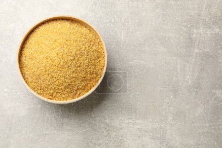 Raw bulgur in bowl on gray table, top view. Space for text