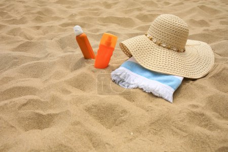 Sunscreens, hat and towel on sand, space for text. Sun protection care