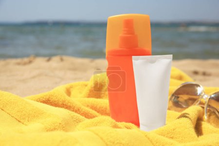 Sunscreen, sunglasses and towel on sandy beach, space for text. Sun protection care