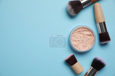 Face powder and makeup brushes on light blue background, flat lay. Space for text