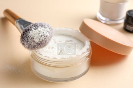 Makeup brush with rice loose face powder on beige background, closeup