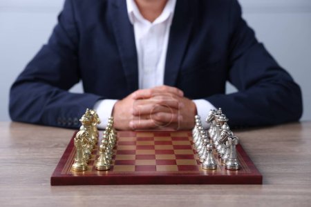 Man with chess pieces on checkerboard at wooden table before game, closeup