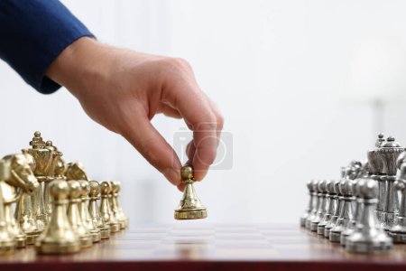 Man with game piece playing chess at checkerboard against white background, closeup