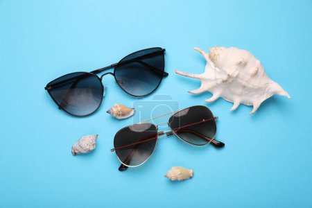 Stylish sunglasses and seashells on light blue background, flat lay
