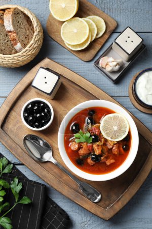Sopa de solyanka de carne con salchichas, aceitunas y verduras servidas en mesa de madera gris, puesta plana