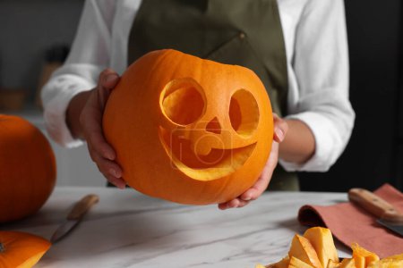 Woman holding carved pumpkin for Halloween at white marble table, closeup