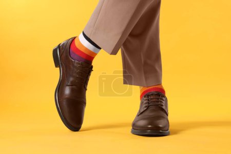Man in stylish colorful socks, shoes and pants on yellow background, closeup
