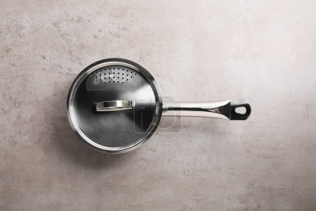 One steel saucepan with strainer lid on light textured table, top view