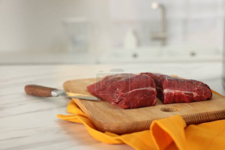 Brett mit Rindfleisch und Messer auf weißem Marmortisch drinnen. Raum für Text