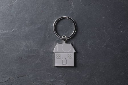 Metal keychain in shape of house on dark textured table, top view
