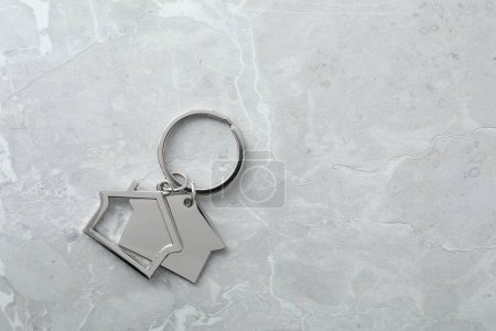 Metal keychain in shape of houses on grey marble table, top view. Space for text