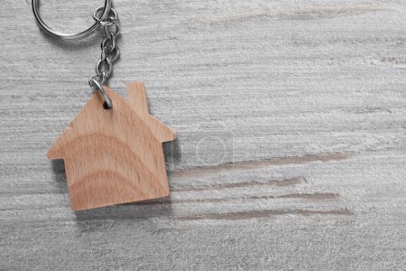 One keychain in shape of house on light wooden table, top view. Space for text