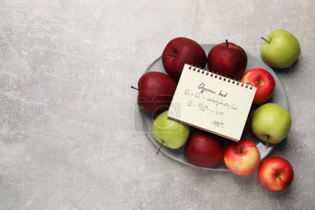 Foto de Cuaderno con carga glucémica calculada para manzanas y frutas frescas en mesa texturizada gris claro, vista superior. Espacio para texto - Imagen libre de derechos