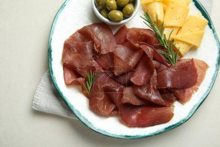 Photo for Delicious bresaola, cheese, olives and rosemary on light textured table, top view - Royalty Free Image
