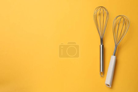 Two metal whisks on yellow background, top view. Space for text