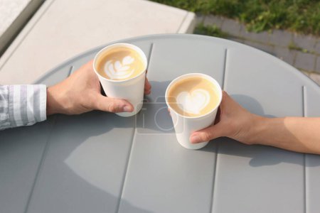Téléchargez les photos : Café à emporter. Couple avec gobelets en papier à table grise à l'extérieur, gros plan - en image libre de droit